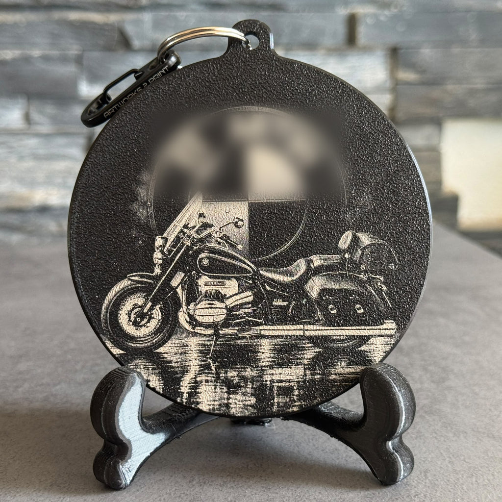 Schwarzer Dubbedeckel mit lasergraviertem Motorrad-Motiv samt Spiegelung, aufgestellt auf einem Ständer – Beispiel für eine Fotogravur